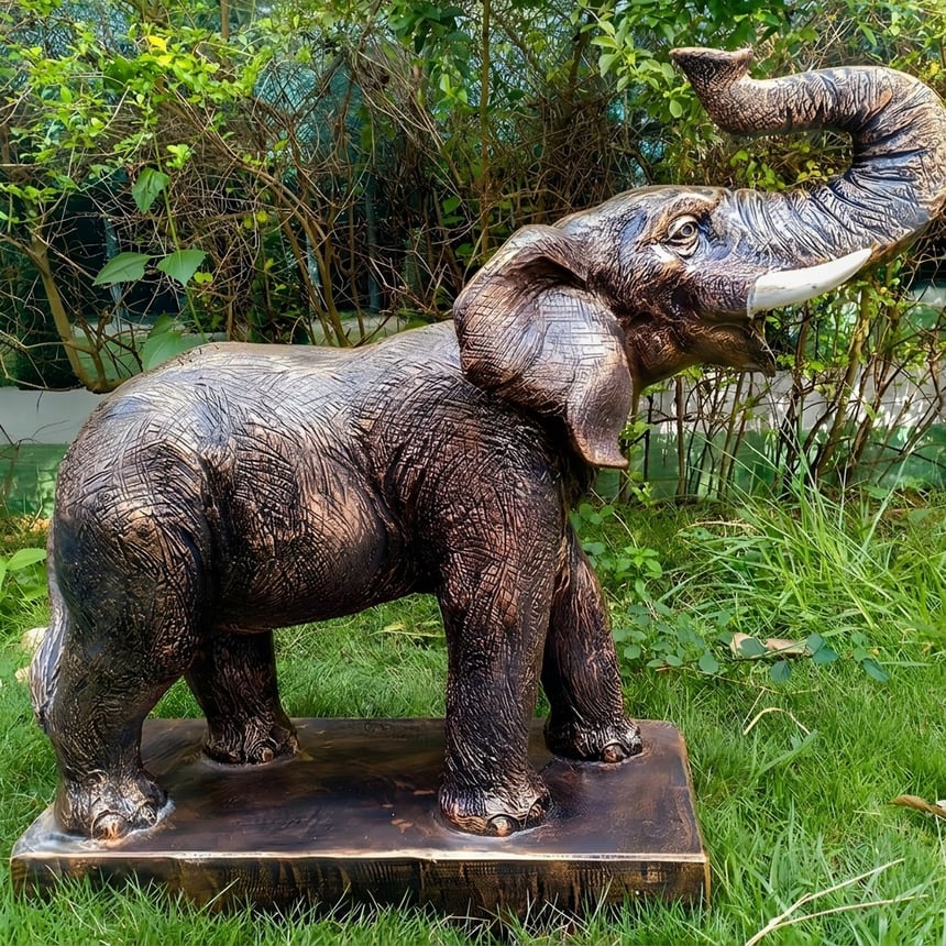 Bronze-finish roaring elephant garden ornament with raised trunk trumpeting in a planted border, a symbol of good fortune