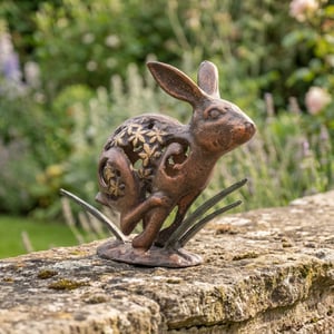 Fretwork rabbit metal garden ornament with rust patina in a cottage garden border