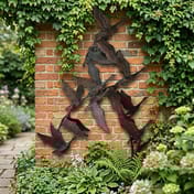 Swans in Flight Metal Ornament mounted on a brick garden wall with climbing ivy
