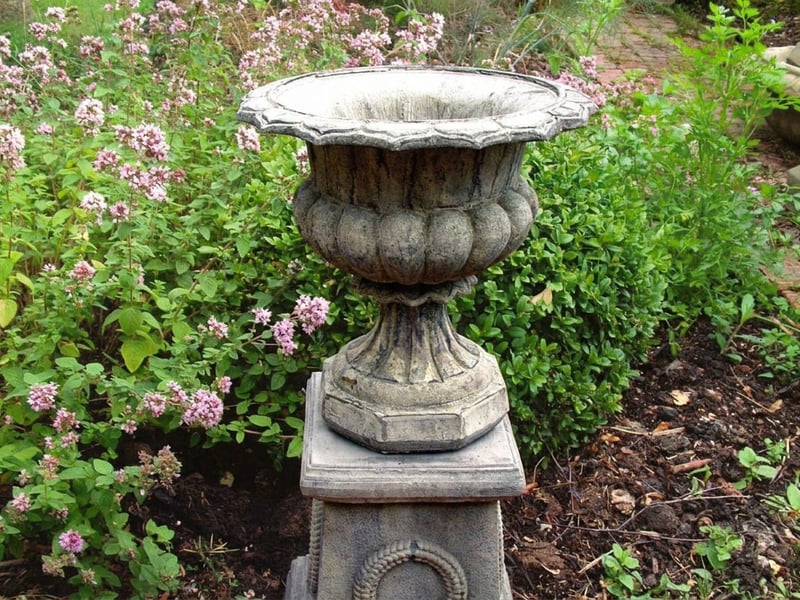 Vienna Laurel Motif Stone Garden Pedestal in a clipped formal garden setting