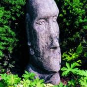 Easter Island Head Statue in garden setting with lush green foliage