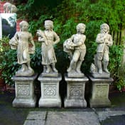 Four Seasons Cast Stone Garden Statues on Decorative Plinths in Garden Setting