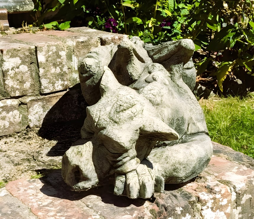 Draco the Dragon cast stone garden ornament in Cotswold stone finish resting on a gravel bed, a bold gift for him