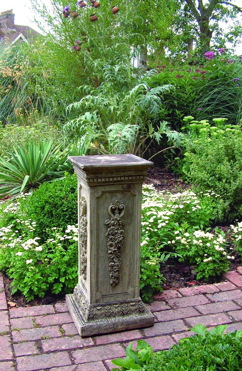 Floral stone garden pedestal with carved flower detail in a cottage garden border