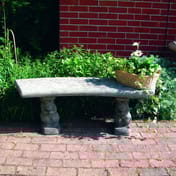 Curved Plain Stone Garden Bench in a garden setting with brick paving and greenery