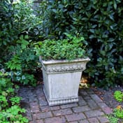 Empire Stone Garden Urn showing scroll motif and lion claw feet in garden setting