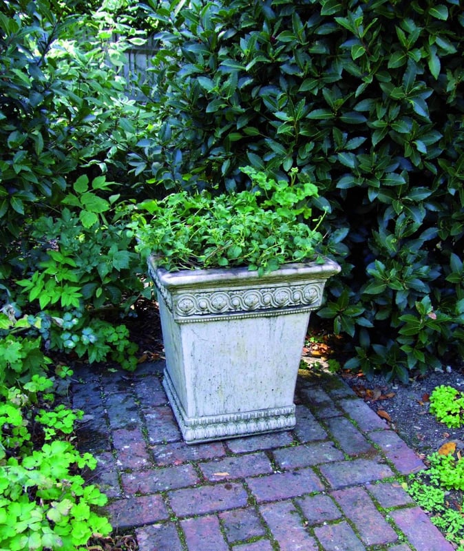 Empire stone garden urn with detailed scrollwork in a stone-walled garden