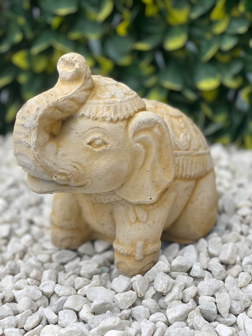 Small Indian elephant stone garden ornament in sandstone with a decorative blanket and raised trunk on a gravel bed