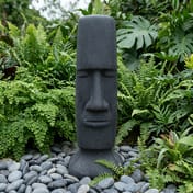 Easter Island Garden Statue in Black in a lush garden setting with ferns and pebbles