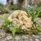 Dragon Hatchling Stone Garden Ornament in Sandstone nestled among ferns and wildflowers in a cottage garden