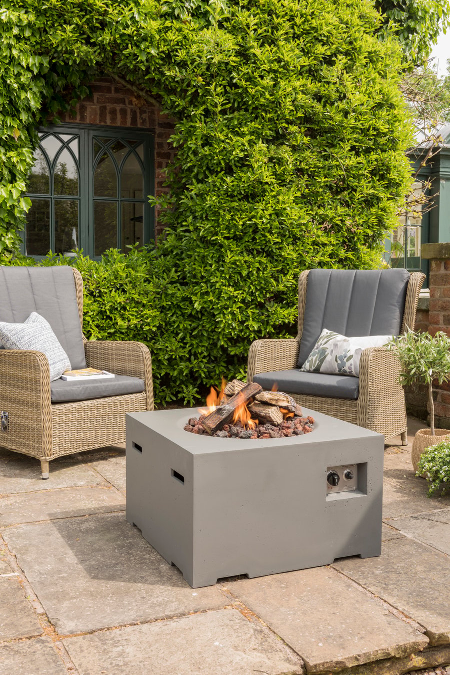 Happy Cocoon 76cm square grey wood-burning fire pit hosting an evening gathering in a UK garden