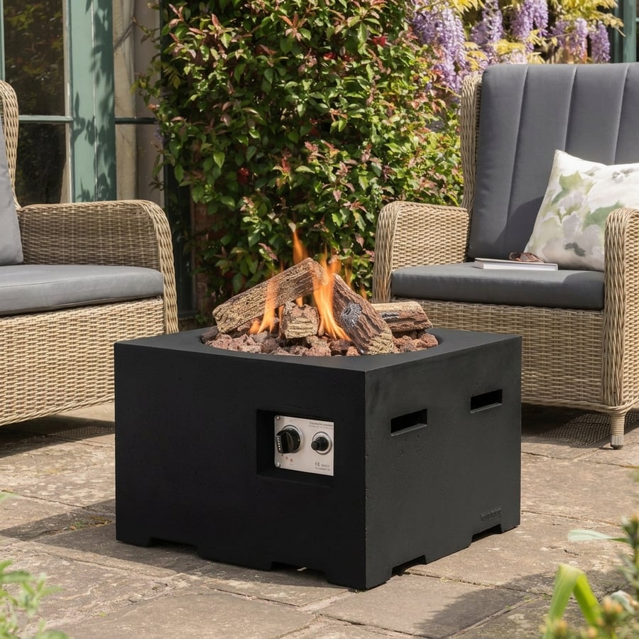 Happy Cocoon 60cm square black wood-burning fire pit in a UK courtyard with Ready to Burn logs stacked nearby