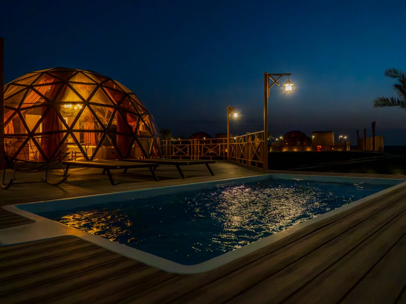 A private pool lit at dusk, the dome glowing behind it against a deep blue sky
