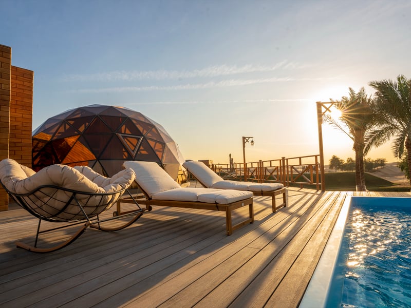 A dome and its private pool at sunset, loungers on the timber deck, palms and dunes behind