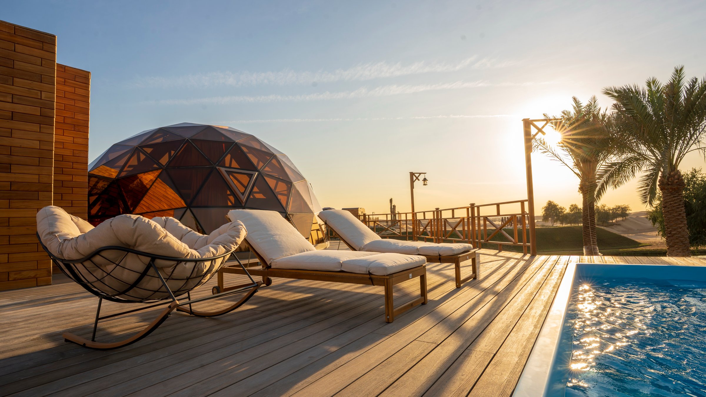 A dome and its private pool at sunset, loungers on the timber deck, palms and dunes behind