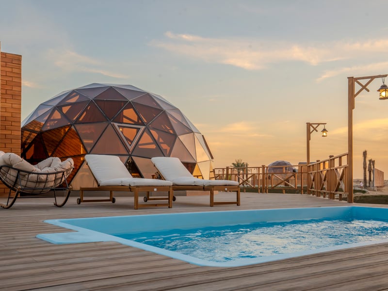 A dome at dusk beside its private pool, lanterns lit along the deck rail