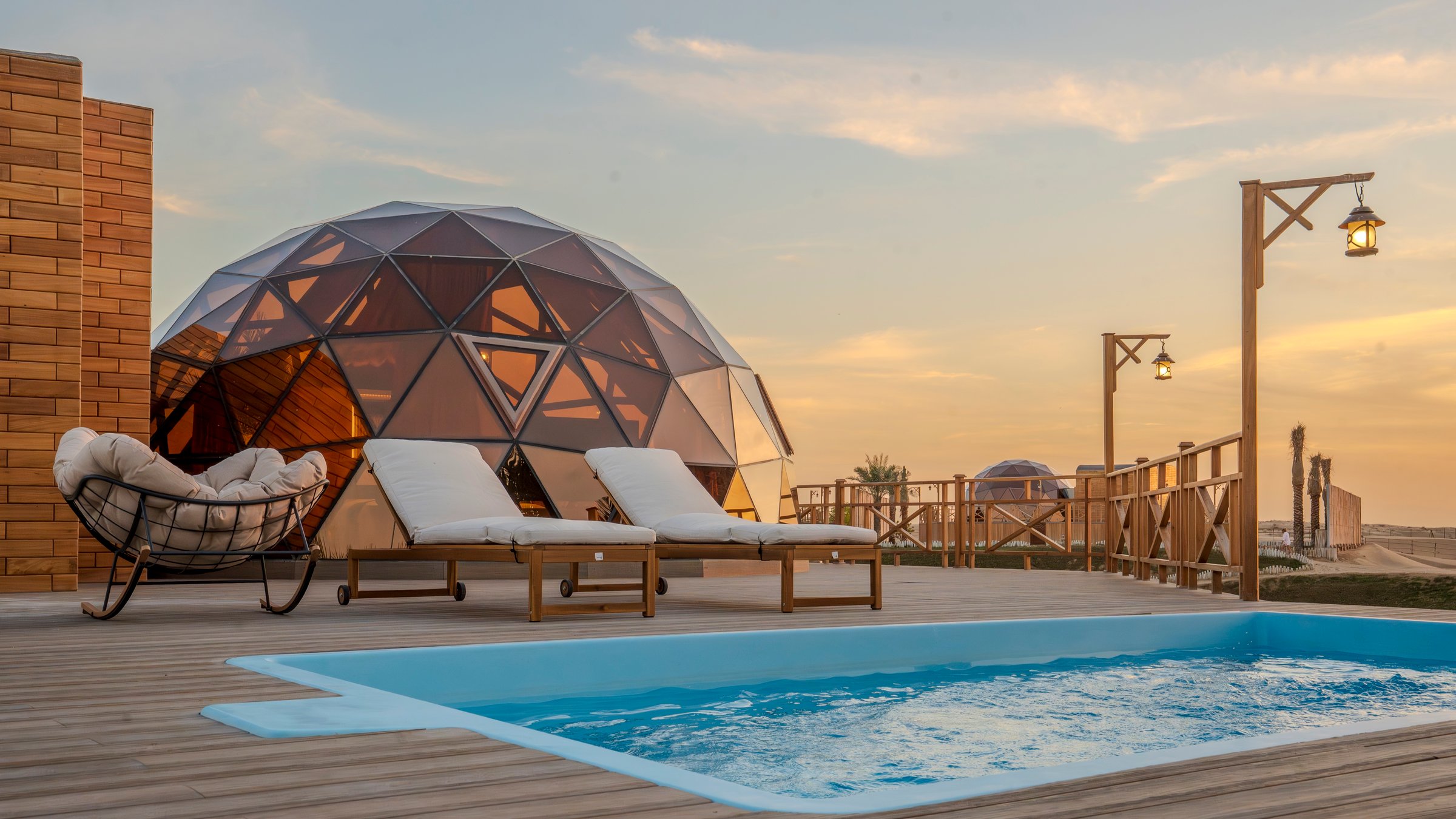 A dome at dusk beside its private pool, lanterns lit along the deck rail