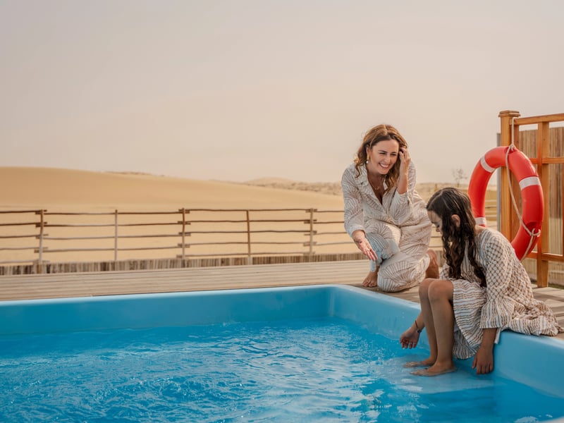 A mother and daughter at the edge of their private pool, the dunes rising behind the deck