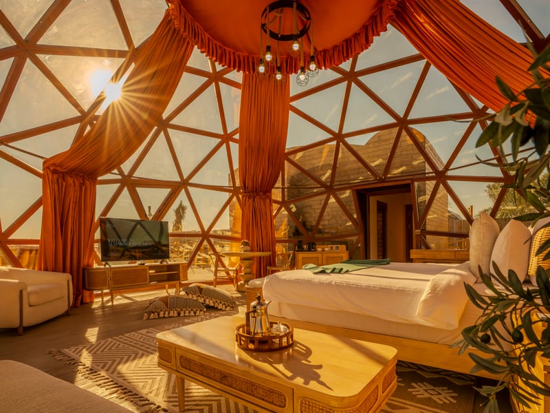 Inside a dome at golden hour, curtains drawn back from the glass and an Arabic coffee set on the table