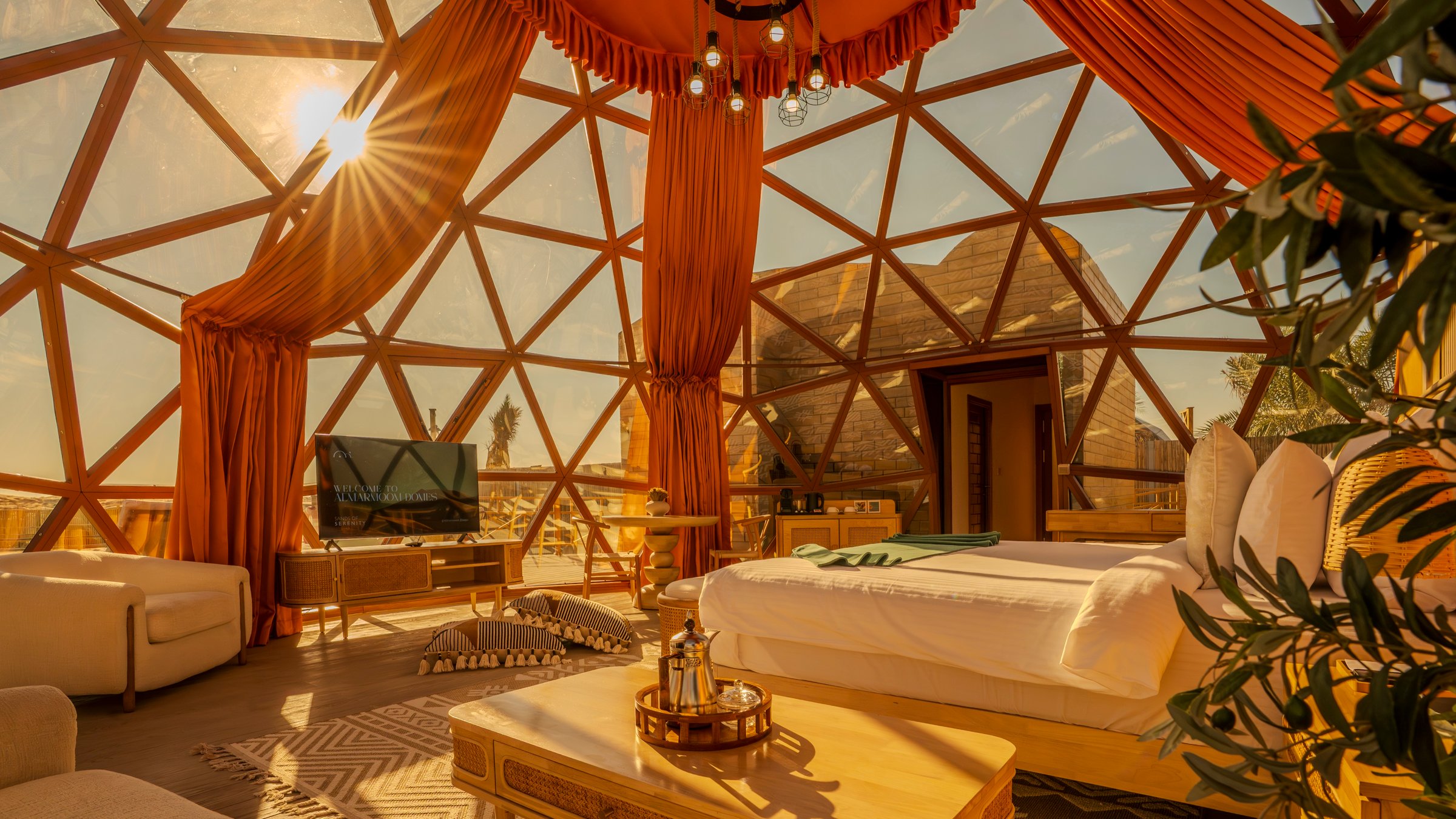 Inside a dome at golden hour, curtains drawn back from the glass and an Arabic coffee set on the table