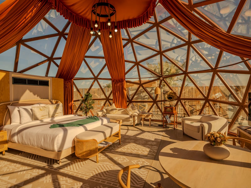 Inside a dome at sunset: the bed and seating under the glass canopy, with the desert beyond