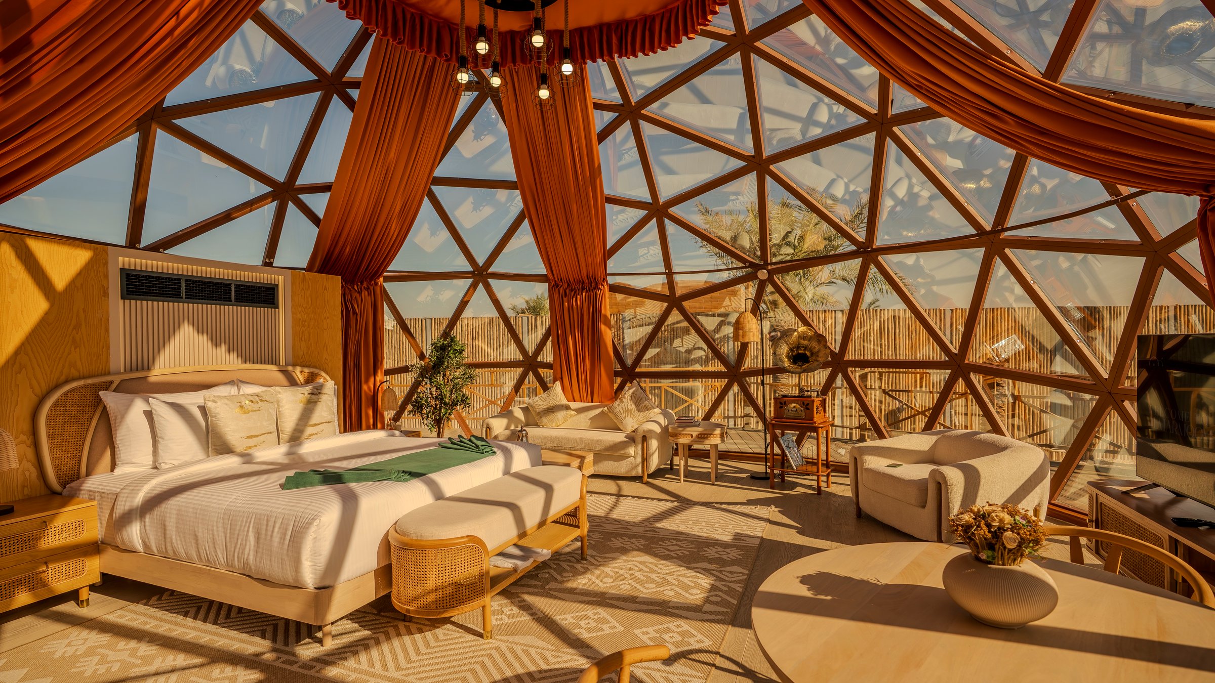 Inside a dome at sunset: the bed and seating under the glass canopy, with the desert beyond