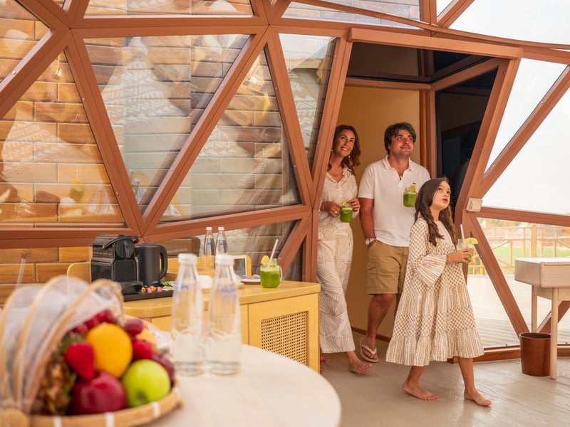 A family with welcome drinks inside a dome, beside a fruit basket and the coffee tray
