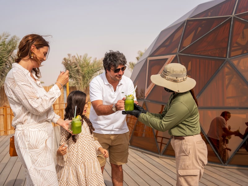 A host handing welcome drinks to a family on the deck outside their dome