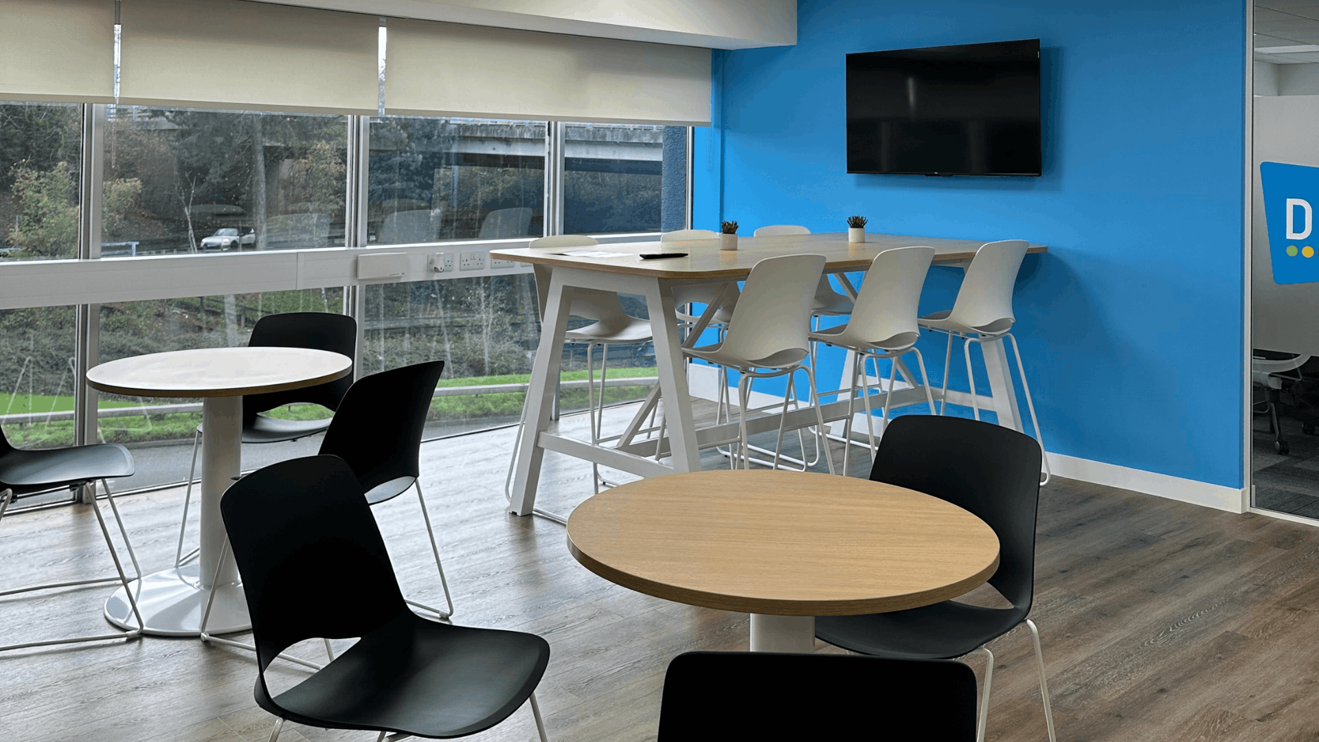 Breakout area completed for the license check office fit out with café tables, black chairs, high bench seating, blue feature wall, wall-mounted tv and large windows