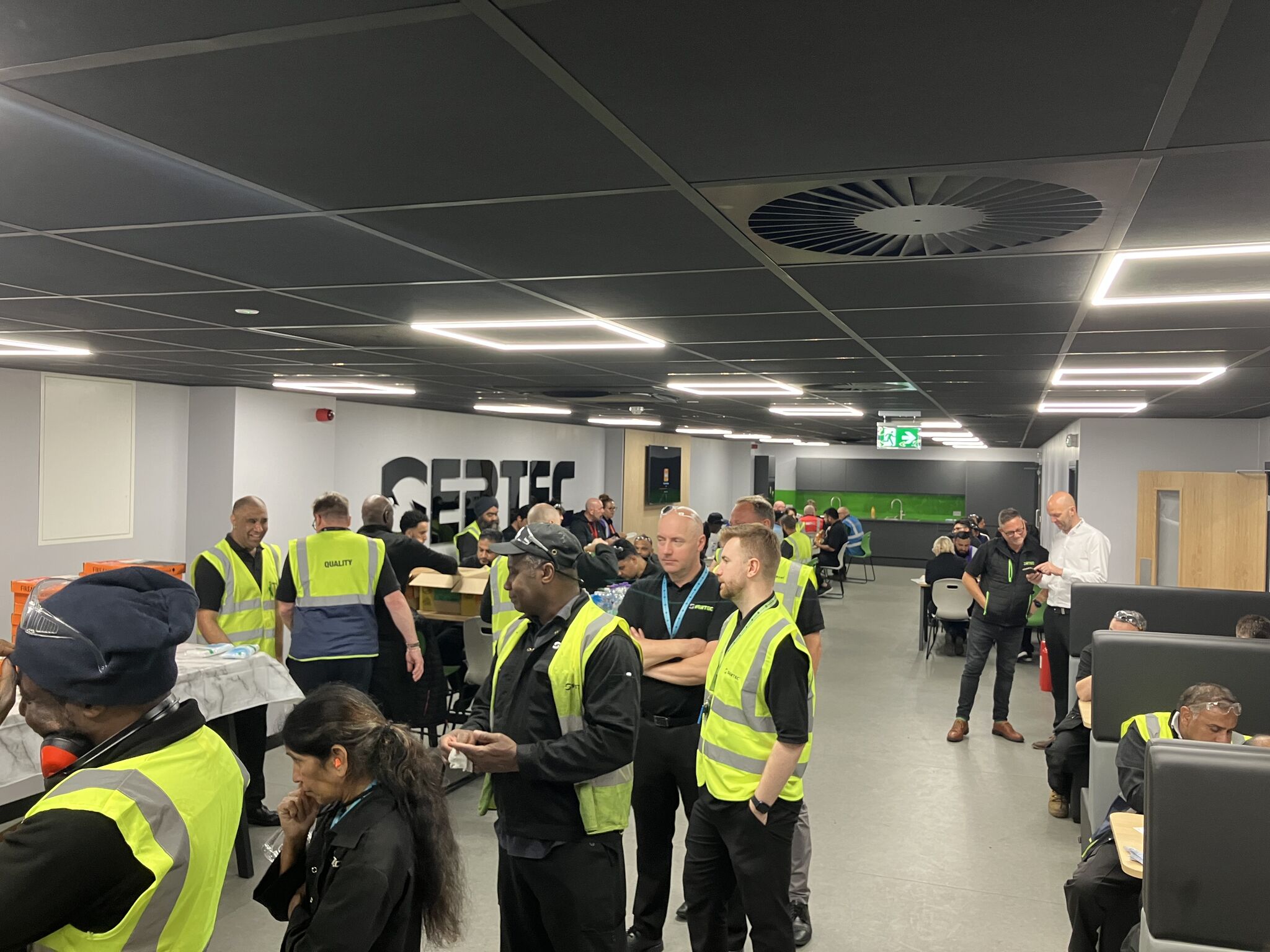 Completed sertec welfare area in use by staff, showing canteen seating, sertec wall branding, black suspended ceiling and new teapoint