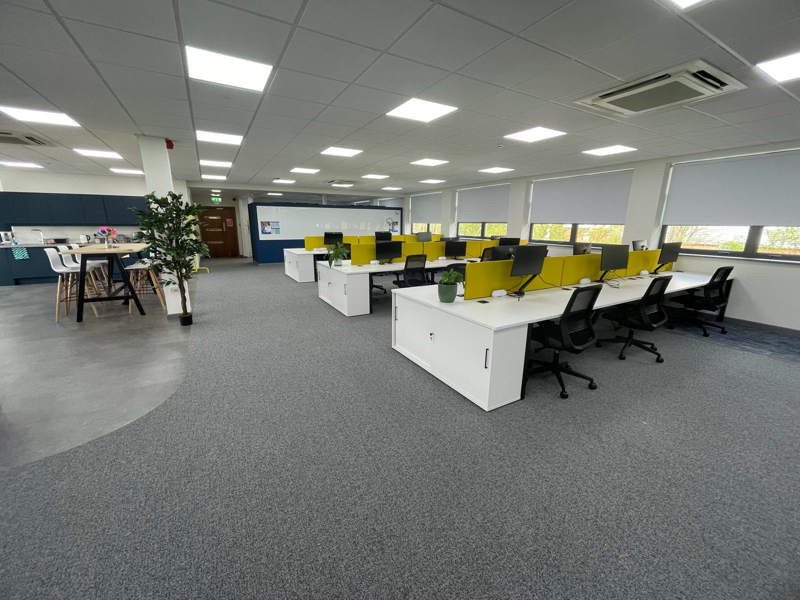 Completed card factory wakefield office refurbishment with open plan desks, teapoint, high table seating and grey carpet flooring