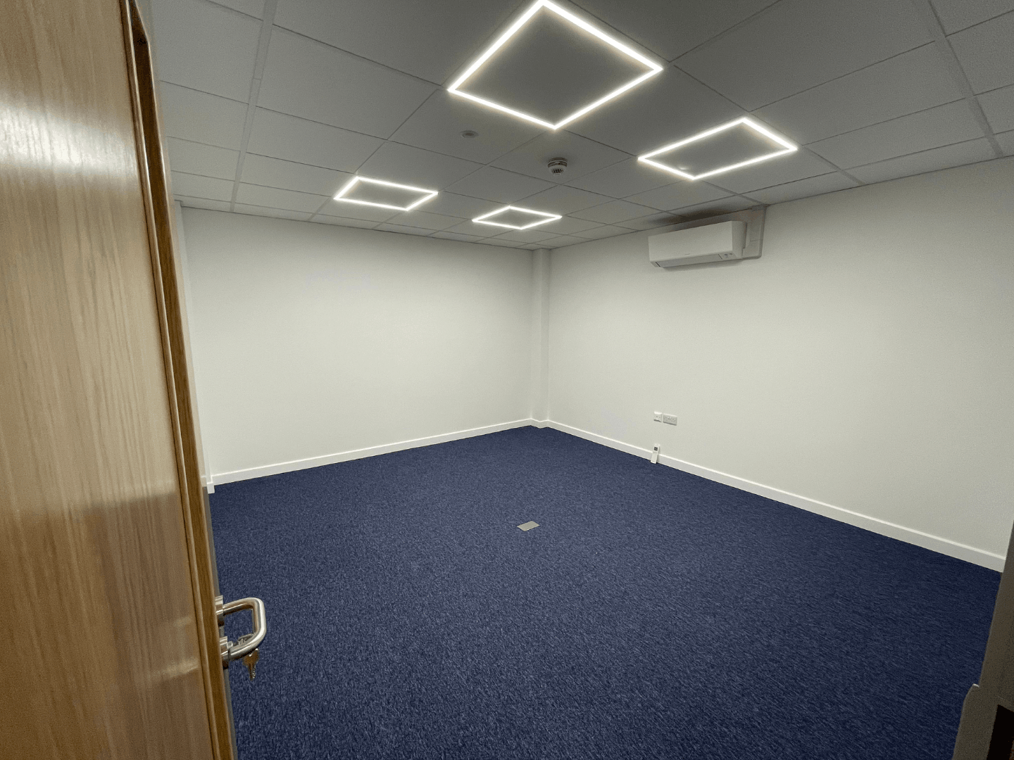 Finished cromwell tools office with blue carpet tiles, suspended ceiling, led lighting and wall-mounted air conditioning