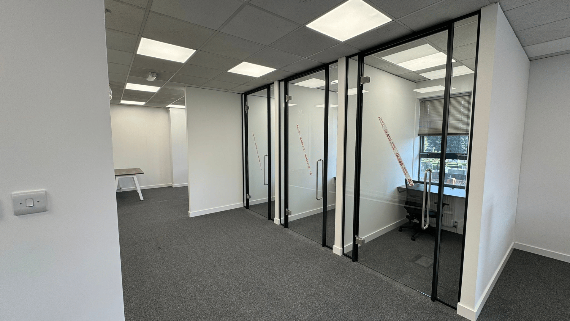 Glass-fronted teams rooms created for the dsl systems office fit out with black framed doors, pull handles and individual workstations inside