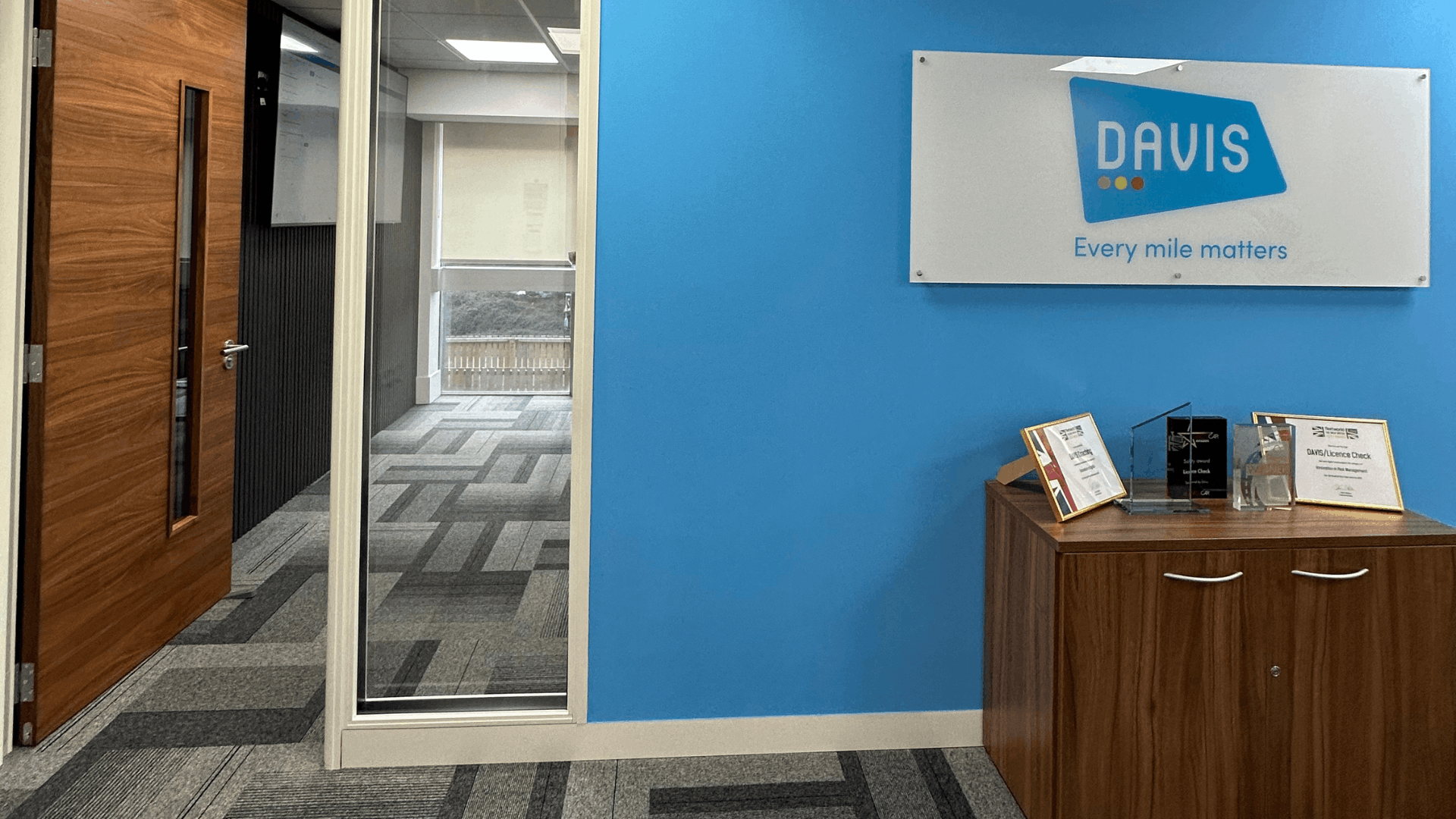 License check office fit out branded wall area with blue feature wall, acrylic davis signage, timber storage cabinet, awards display and glazed meeting room entrance