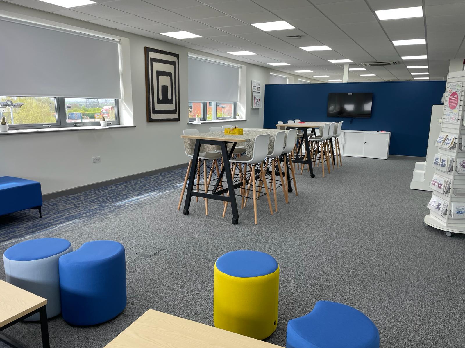 Agile working area at card factory wakefield with high meeting tables, white chairs, blue feature wall and product display stands