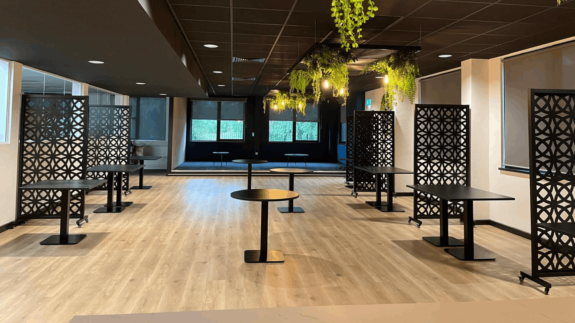 Riviera travel breakout area with black tables, privacy screens, timber flooring and suspended planting