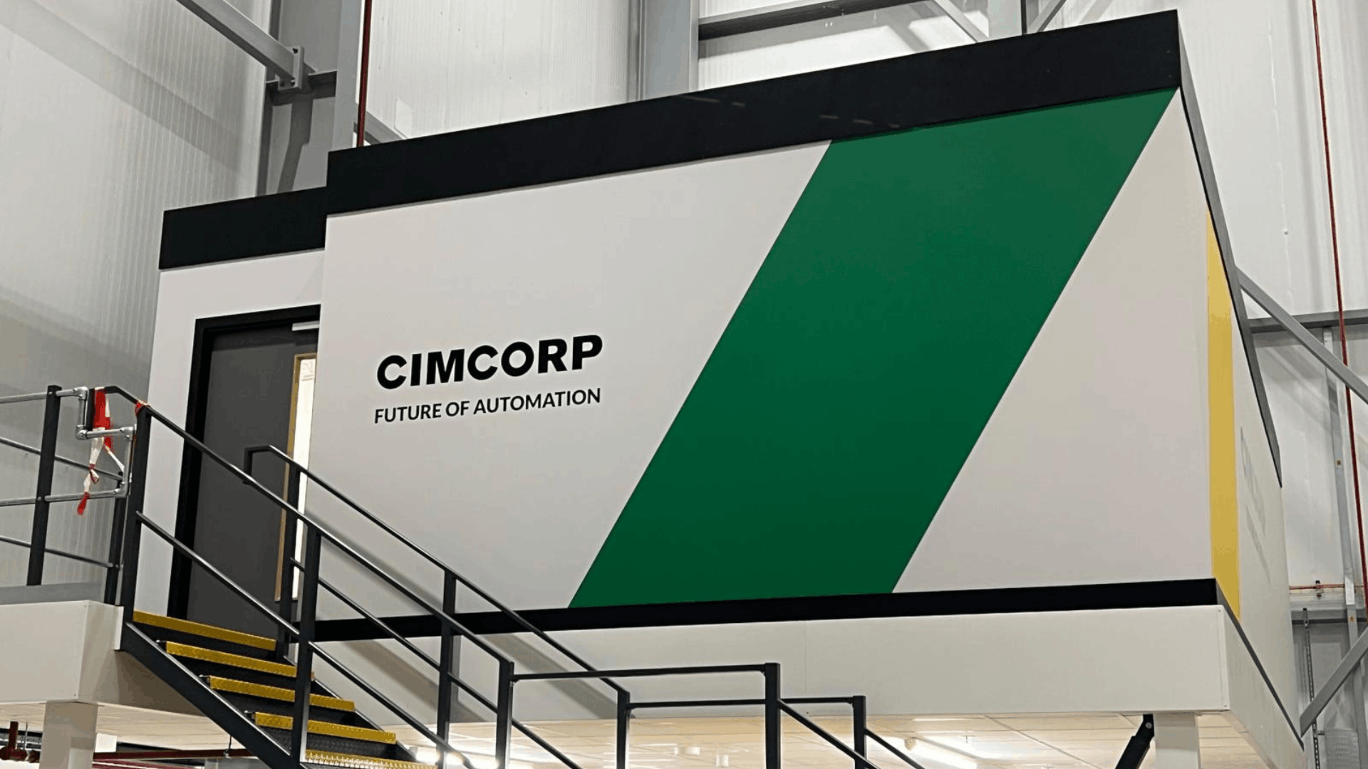 Close-up of cimcorp branded mezzanine office exterior with green wall graphic, black steel staircase and industrial warehouse backdrop