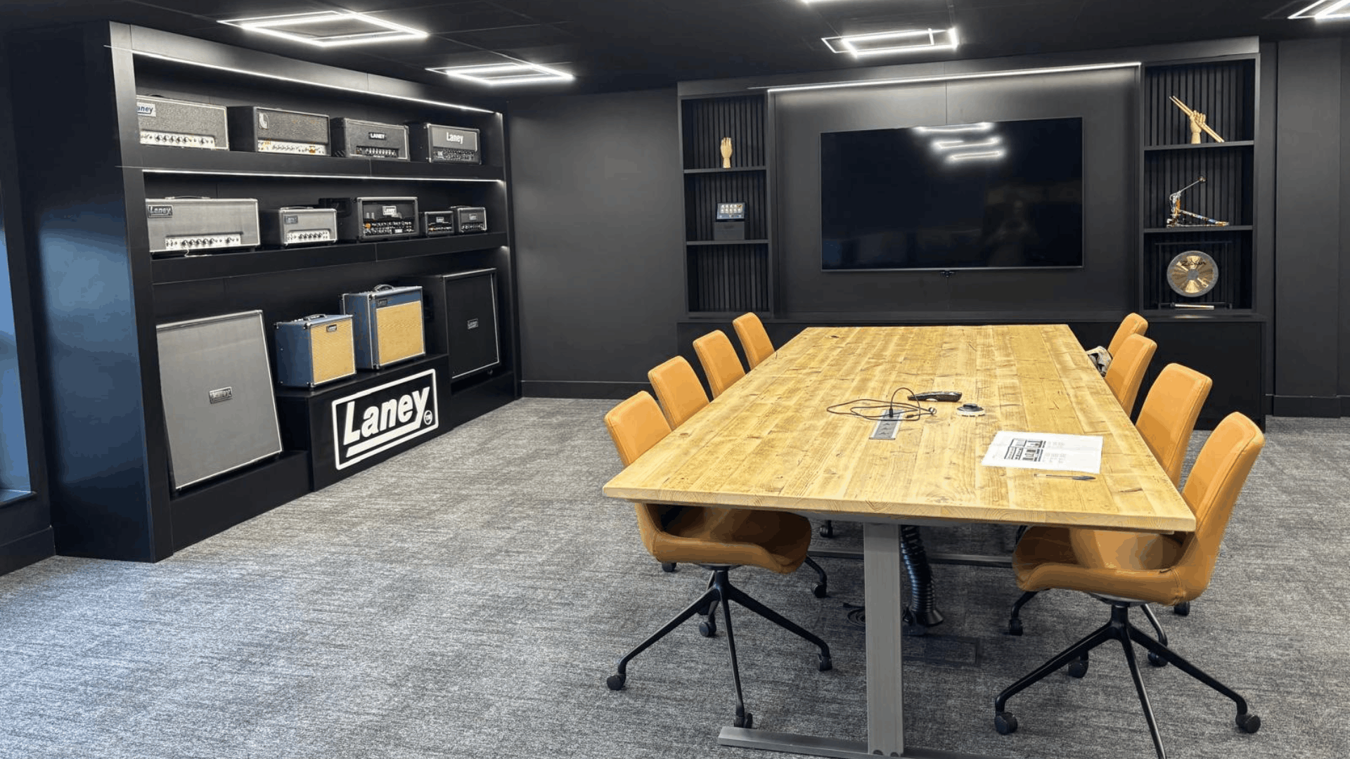 Finished headstock group boardroom with bespoke media wall, amp display shelving, timber meeting table and tan chairs