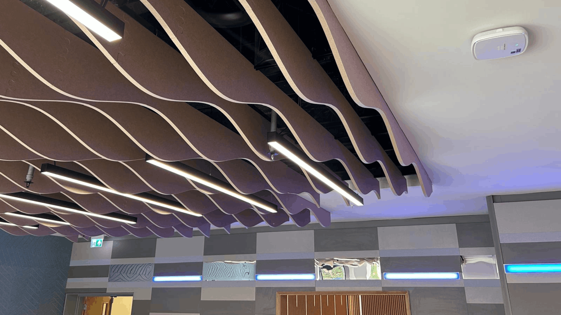 Wave-style acoustic ceiling panels with suspended linear lighting in the refurbished nec media suite