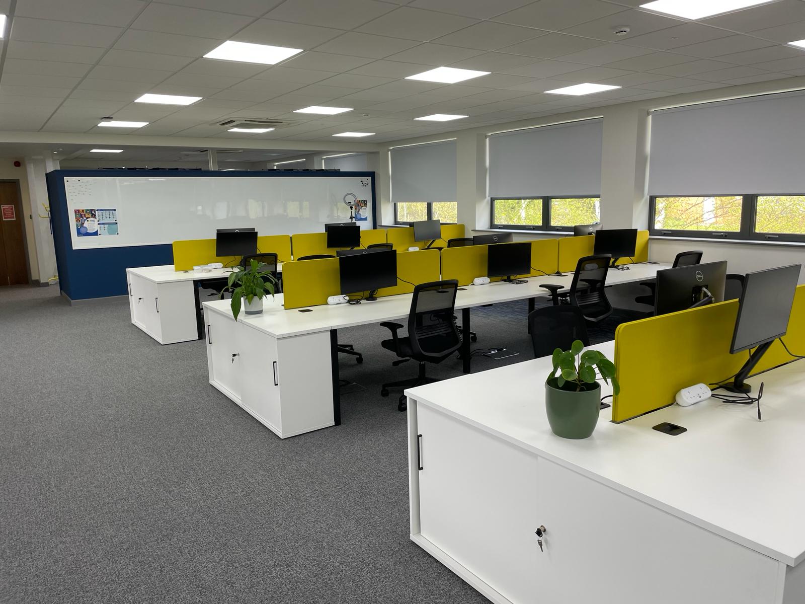 Open plan office area at card factory wakefield showing white bench desks, yellow desk dividers and a large magnetic write on wall