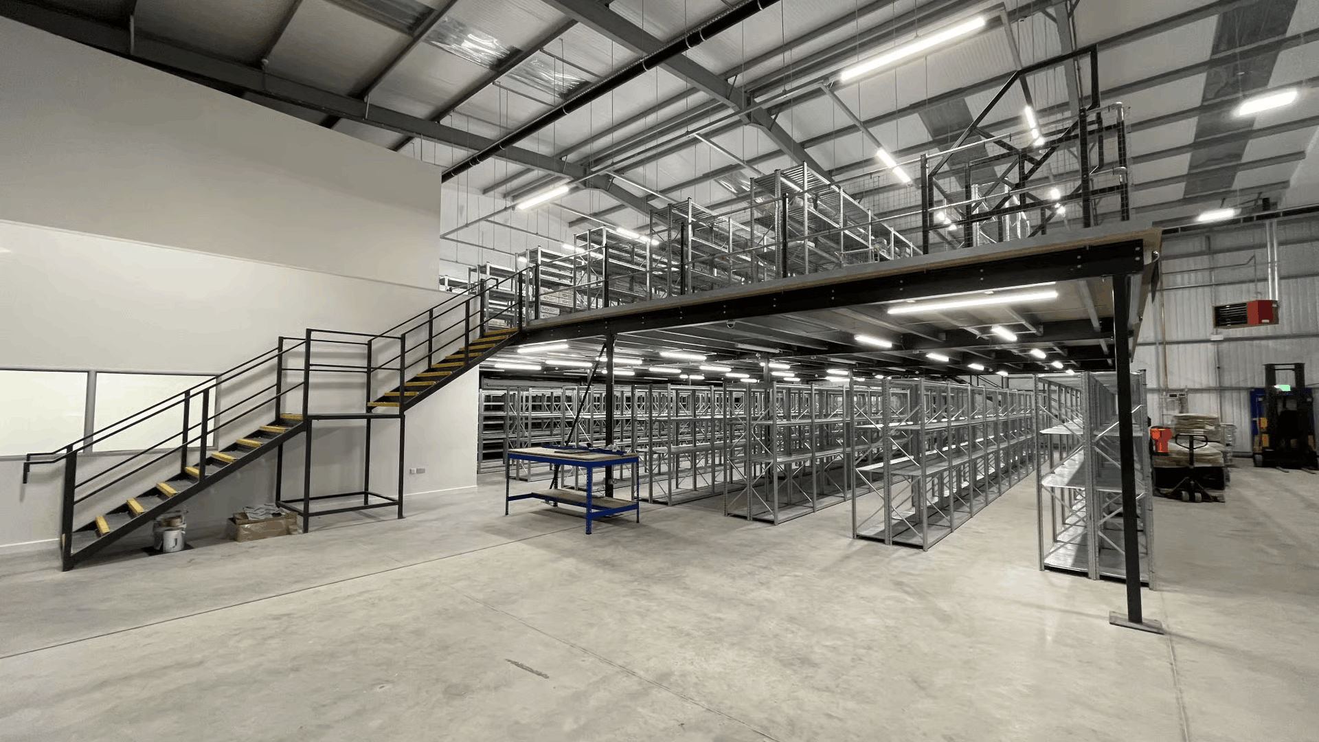 Industrial workspace refurbishment with mezzanine floor, warehouse racking, safety stairs, and overhead lighting