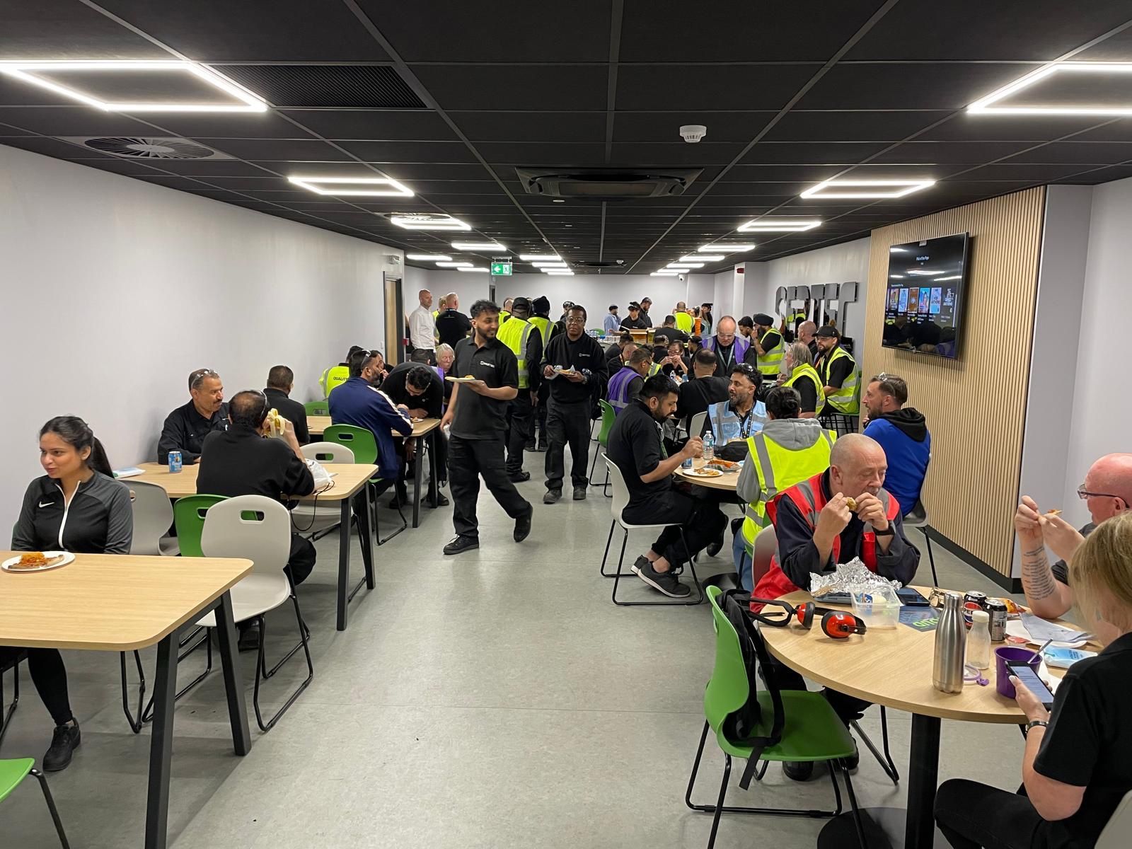 Sertec staff using the refurbished welfare area with canteen tables, green chairs, timber feature wall and black suspended ceiling