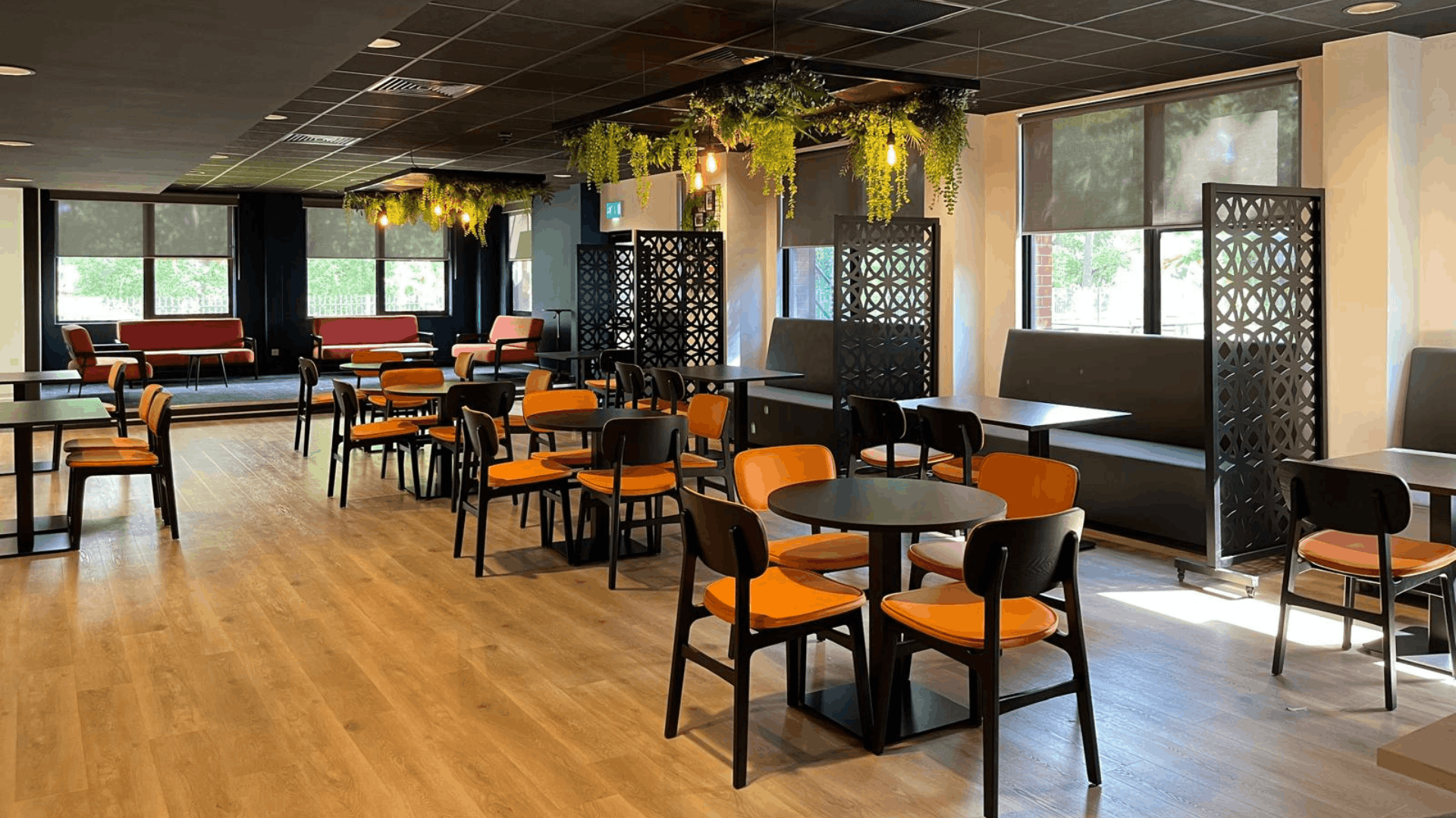 Riviera travel breakout area with orange seating, black decorative screens and suspended planting features