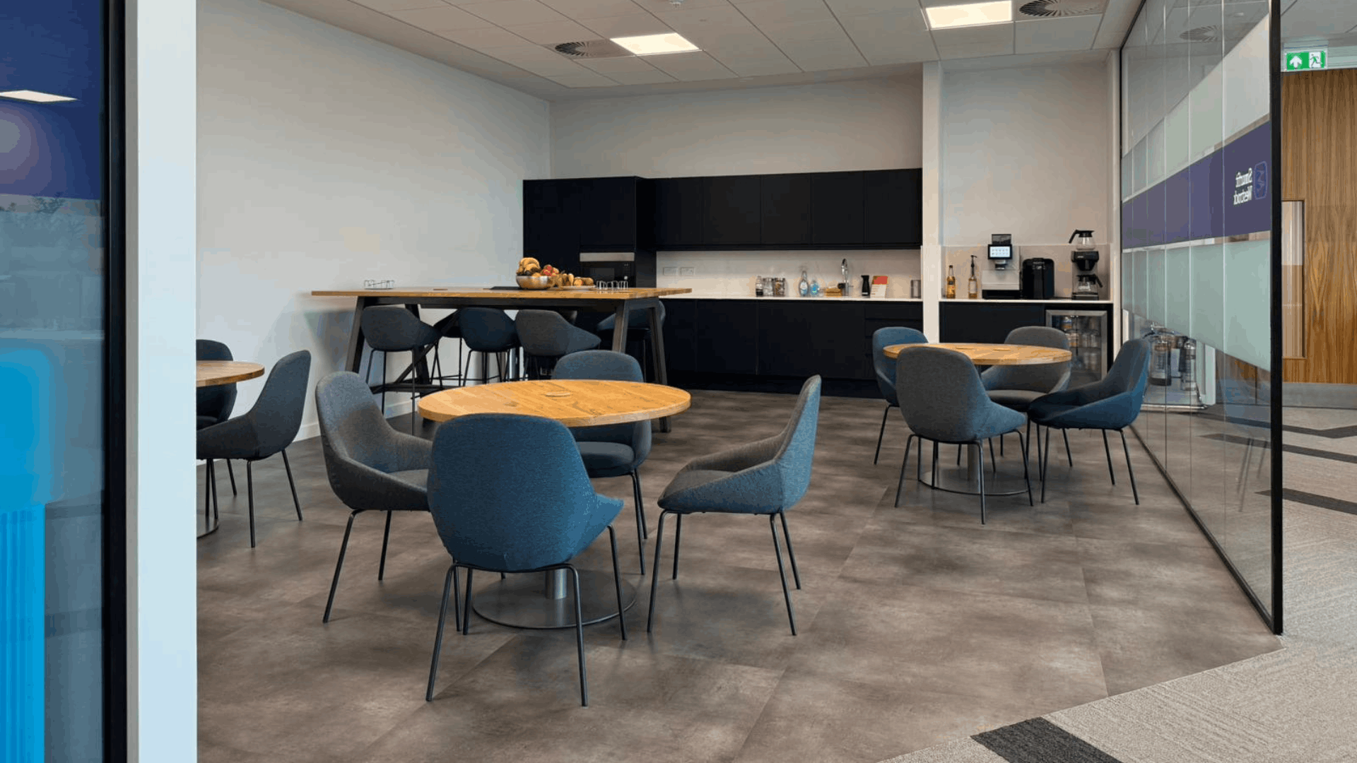 Smurfit westrock breakout space with black tea point, timber tables, upholstered chairs and glass partitions