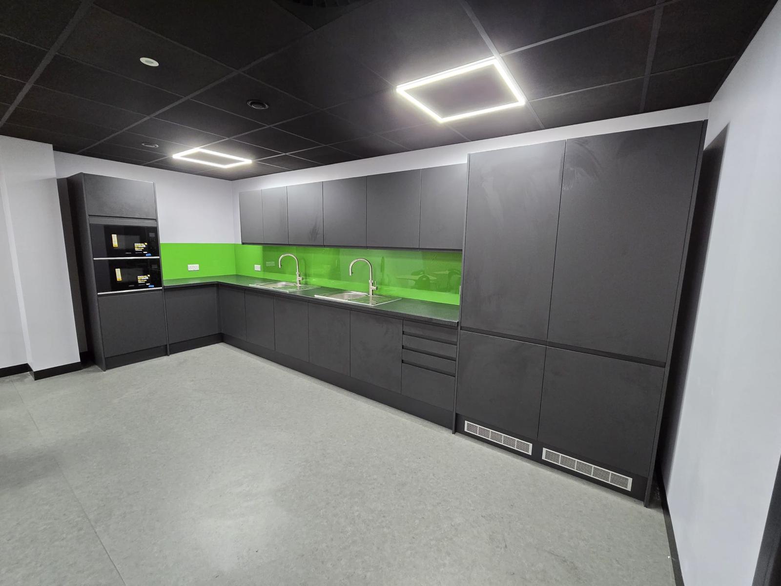 New teapoint in the sertec welfare area refurbishment with dark kitchen units, green acrylic splashback, integrated microwaves and stainless steel sinks