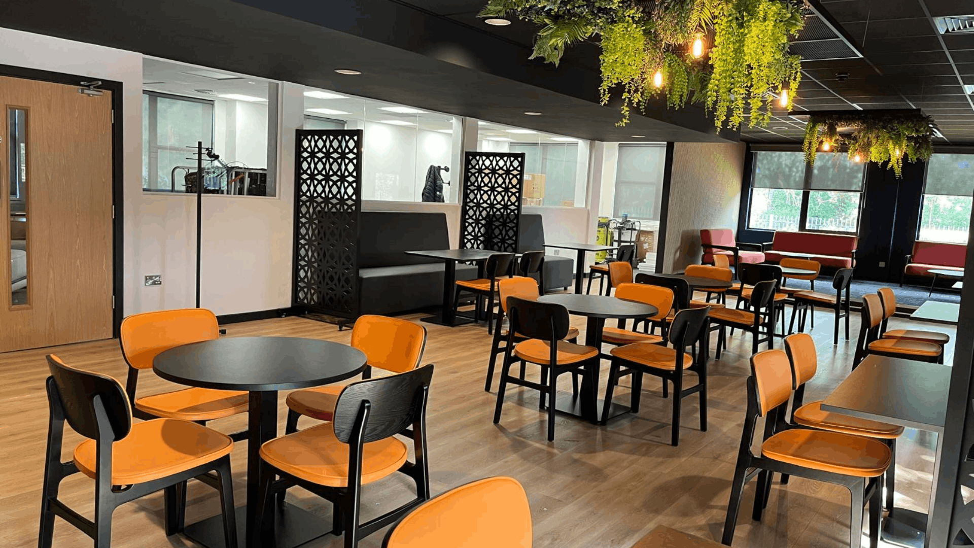 Riviera travel staff breakout area with orange chairs, black tables, booth seating and feature ceiling rafts