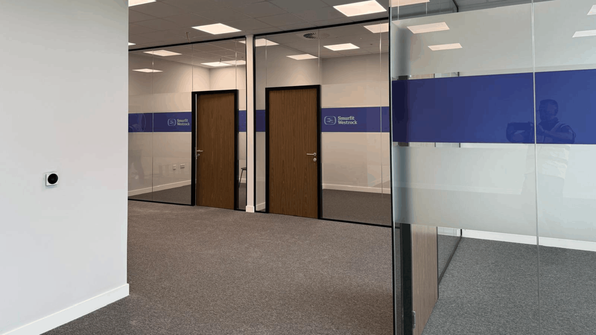 Glass partitioned offices at smurfit westrock with branded manifestation and walnut veneer doors
