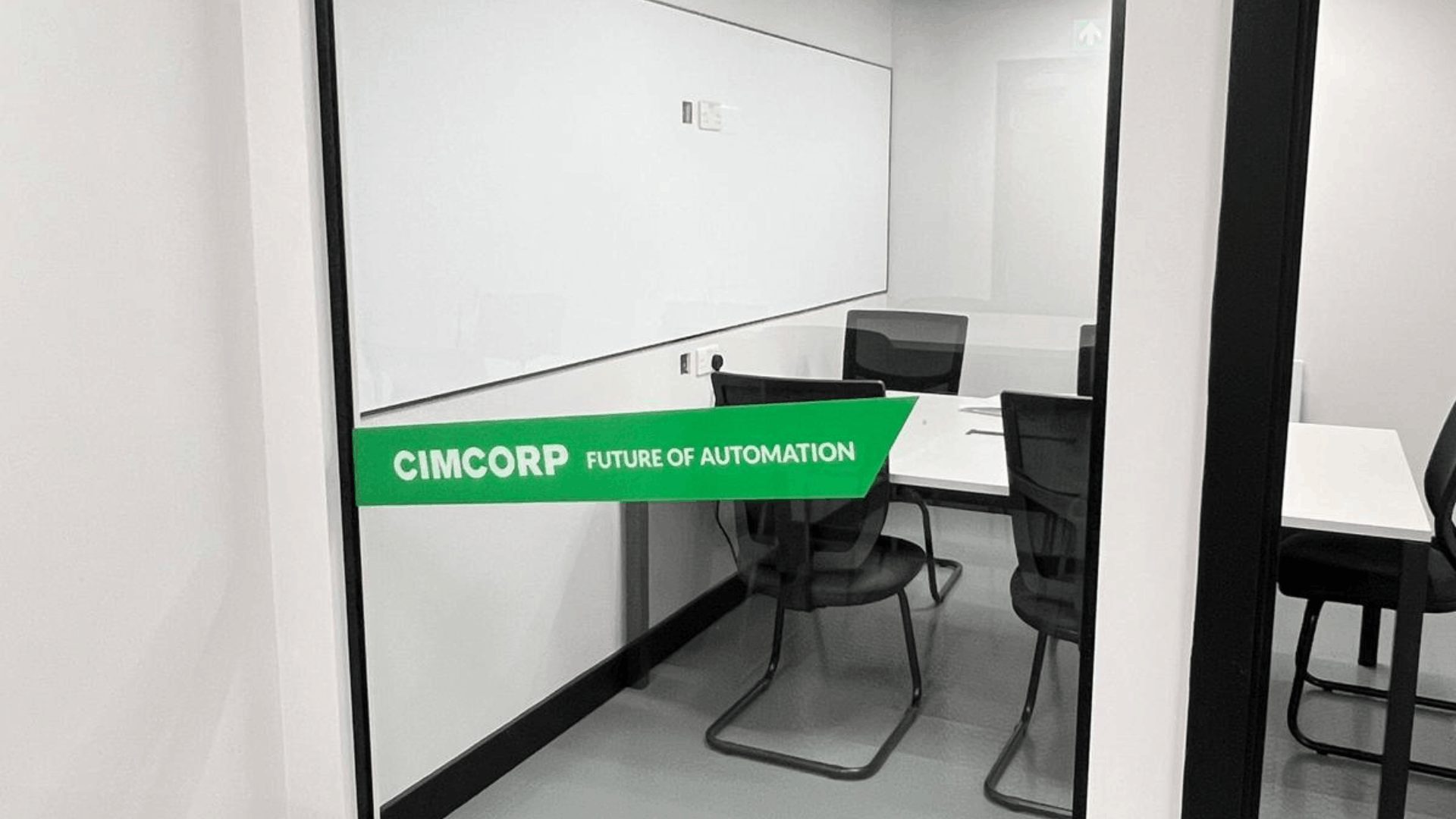Glass partition entrance to cimcorp mezzanine meeting room with green branded manifestation, black door frame, rubber flooring and write-on wall surface inside