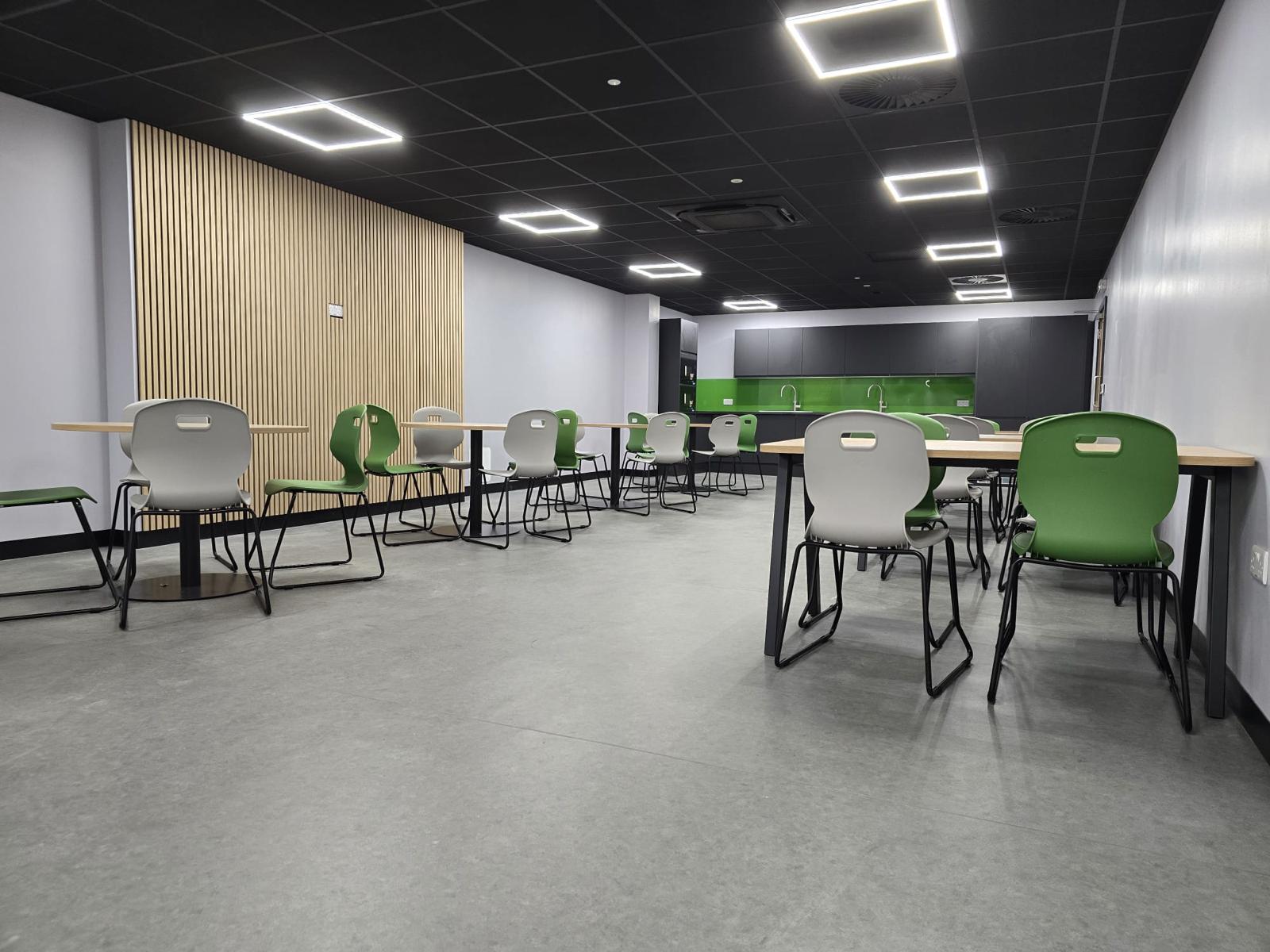 Refurbished sertec welfare area in birmingham with canteen seating, black suspended ceiling, square led feature lighting, green splashback and timber slat wall