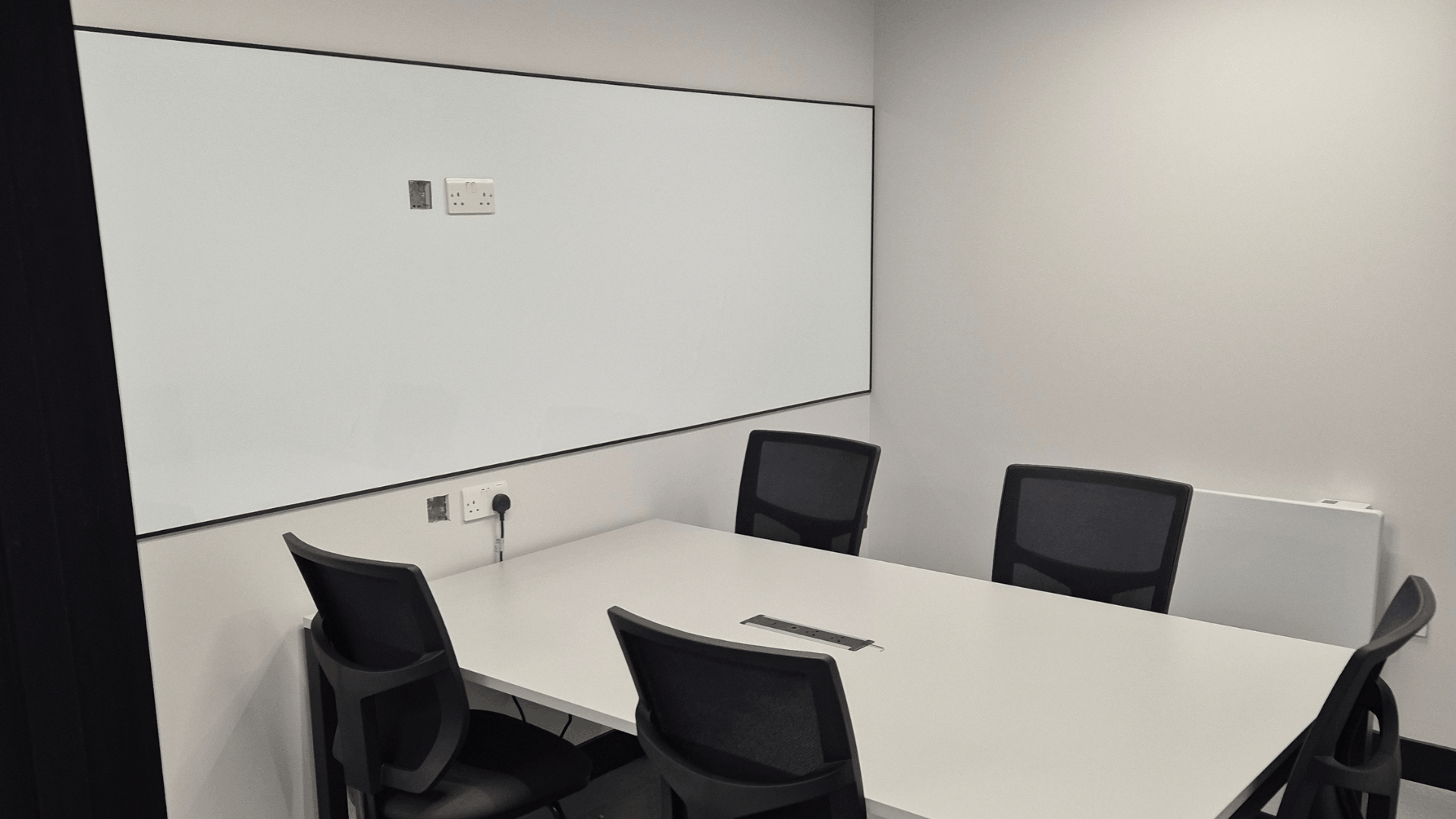 Cimcorp mezzanine meeting room with white meeting table, black chairs, write-on wall vinyl, grey rubber flooring and black ceiling tiles with led lighting